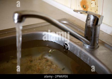 Stainless steel sink plug hole close up full of water and particles of food. Overflowing kitchen sink, clogged drain. Problems with the water supply Stock Photo