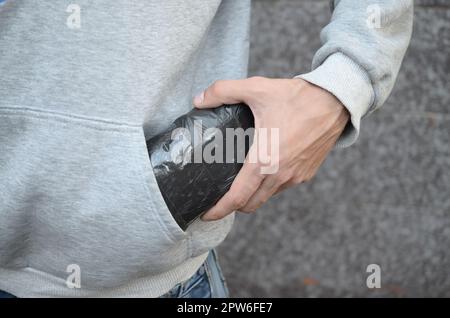 Drug dealer taking bag with cocaine out of hoodie pocket on dark tiles background close up. Narcotic trafficking concept. Drug addiction Stock Photo