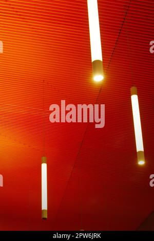 Intense orange ceiling with vertical light tubes. Modern architecture, interior. Stock Photo