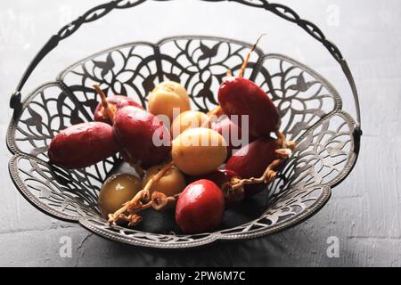 Red and Yellow Raw Dates Fruit or Kurma Muda (Ruthob) on Vintage Basket Above Rustic Background. Stock Photo