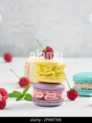 Stack of multicolored macaroons and red raspberries on a white background Stock Photo