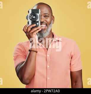 One happy African American man standing against a yellow background in a studio and taking pictures on a camera. Confident cheerful black man holding Stock Photo