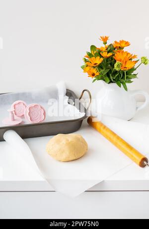 Preparation of the dough for making cookies with molds in the form of flowers, a rolling pin, a bouquet of orange flowers and a baking tray. Concept o Stock Photo