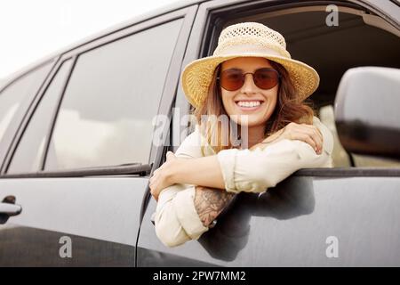 Portrait of One beautiful young brunette caucasian woman hanging out the window of a car while taking a road trip, travelling to her destination. Attr Stock Photo