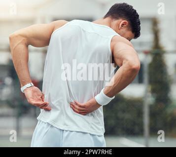 Rearview unknown mixed race tennis player suffering from backache in court game. Hispanic fit athlete in pain while holding and rubbing back injury in Stock Photo