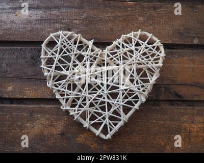A heart woven from rustic light rods or threads. Wicker form handmade. Valentine's Day. Postcard. Wooden texture background. Love concept. Stock Photo