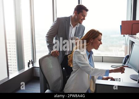 Were putting our heads together on this one. man standing behind a woman as she works on her computer. Stock Photo