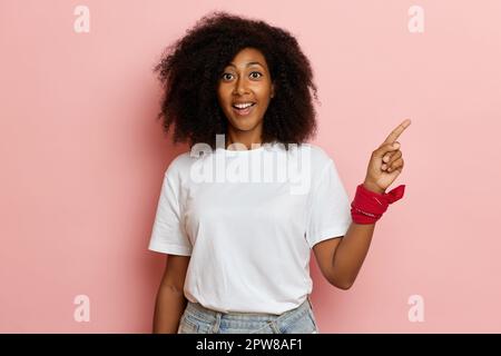 Cute curly haired female smiling positively and shows finger to copy space. High quality photo Stock Photo