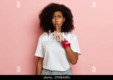 Young dark skin woman shows silence sign, she wants to be quiet and not make noise. Stock Photo