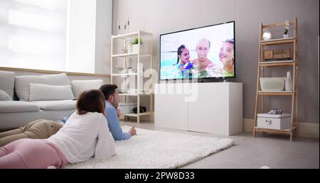 Young Couple Watching TV While Sitting On Sofa In Living Room At Home Stock Photo