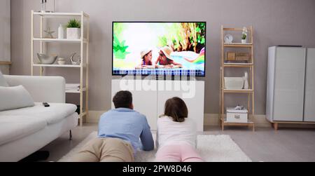 Young Happy Couple Lying On Carpet Watching Movie On Television At Home Stock Photo