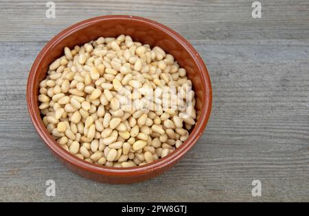 Pine nuts in a small ceramic bowl on rustic wooden board Stock Photo