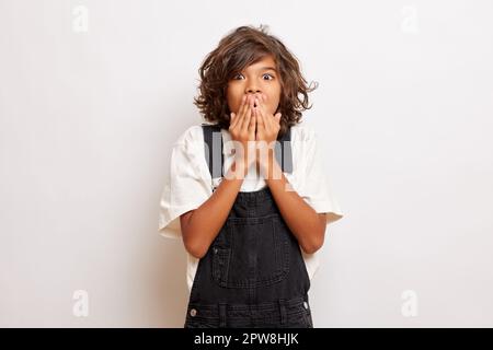 Studio shot of shocked emotional young guy covers mouth with hands, tries to be silent, poses over white background. High quality photo Stock Photo