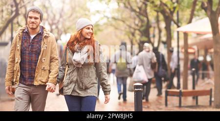 Happy couple, holding hands and walking in city together in winter for romance or travel outdoors. Man and woman having a walk or stroll in park or Stock Photo