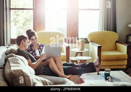 Making bill paying an enjoyable experience. a young couple using a laptop and going through paperwork together on the sofa at home. Stock Photo