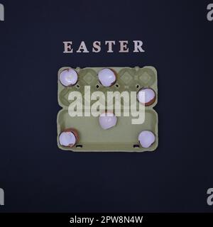 Egg shells arranged in an egg box on a black background with the inscription Easter. Minimalistic life style scene. Stock Photo
