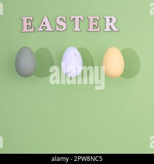 Three Easter eggs of different colors with a stronger shade and the inscription Easter made of wood on a light green background with copy space. Minim Stock Photo