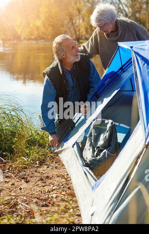 Its the perfect spot to pitch their home. a senior couple setting up a tent while camping in the wilderness. Stock Photo