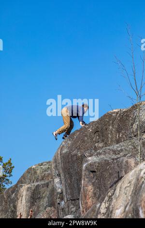 Boulderer or rock climber reaching the top of a cliff against clear blue sky at Humallahdenkalliot in Meilahti district of Helsinki, Finland Stock Photo