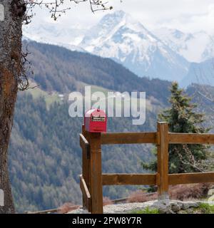 Red post box on a wooden fence in the alpine town of Lignan in the Aosta Vally, NW Italy Stock Photo