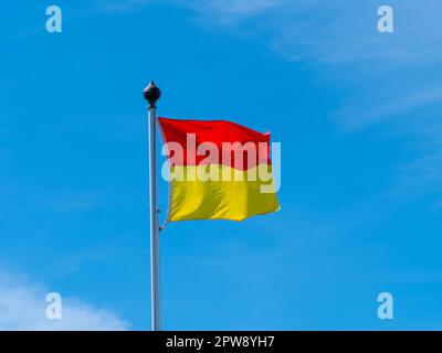 A red and yellow flag allowing swimming on the beach. flag on a blue sky background. Stock Photo