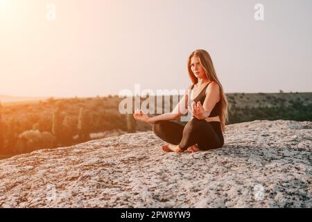Fitness woman. Happy middle-aged fitness woman doing stretching and pilates on a rock near forest at sunset. Female fitness yoga routine. Healthy Stock Photo