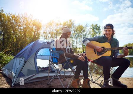 Music is only love looking for words. a young man playing his girlfriend a song on his guitar while out camping. Stock Photo