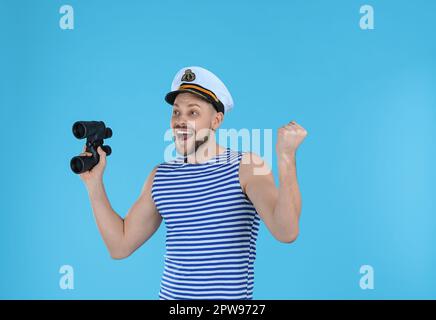 Happy sailor with binoculars on light blue background Stock Photo