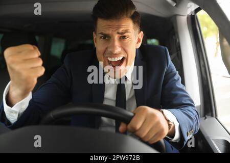 Emotional man yelling in car. Aggressive driving behavior Stock Photo