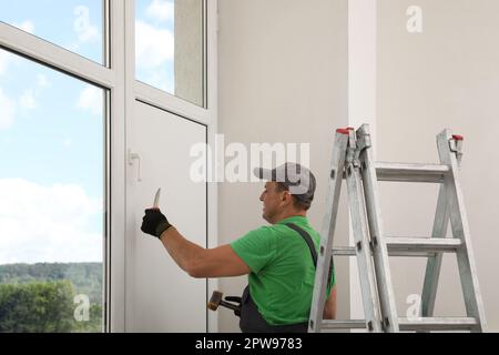 Worker holding knife and hammer indoors. Window installation Stock Photo