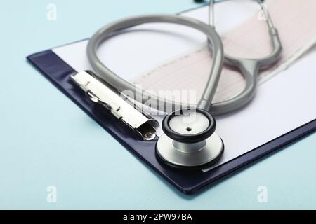 Clipboard with stethoscope and cardiogram on turquoise background, closeup Stock Photo