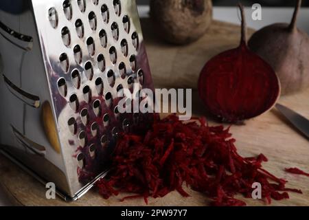 Grater and fresh ripe beetroot on wooden board, closeup Stock Photo