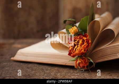 Open book with folded pages and beautiful dried flowers on wooden table, closeup Stock Photo