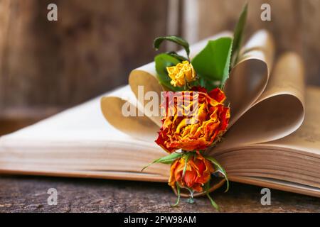 Open book with folded pages and beautiful dried flowers on wooden table, closeup Stock Photo