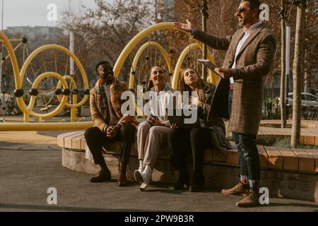 Older business man showing something to his colleagues while they are sitting on the wooden bench Stock Photo