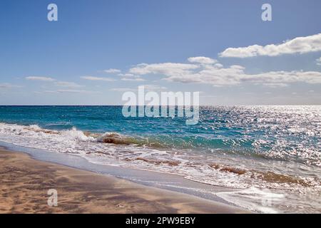 Sandy beach coastline in Fuerteventura, with turquoise blue water and gentle waves crashing onto the shore Stock Photo