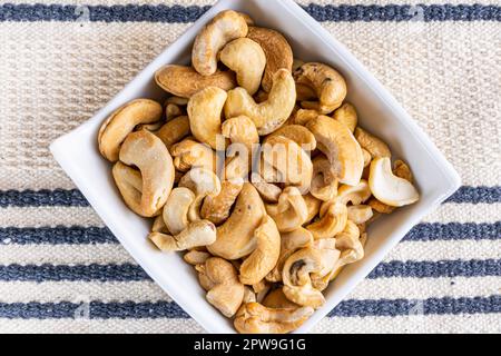 Cashew nuts in crockery jar on blue and white striped fabric background. Stock Photo
