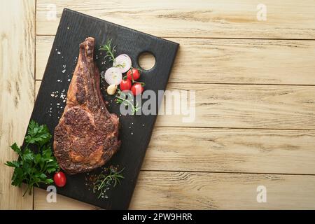 Tomahawk steak. Sliced grilled tomahawk beef steak with baked cherry tomatoes, herbs and salt on old wooden background. Preparing to grill.  Top view Stock Photo