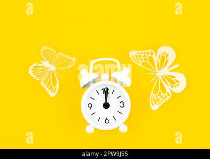 White alarm clock and paper butterflies on a yellow background. Stock Photo