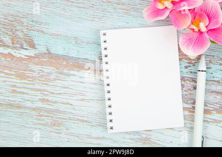 Empty notebook with white pages and bright pink orchid flowers on blue wooden background. Stock Photo