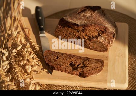 Fresh, brown, freshly baked, multi-grain and yeast-free bread on a cutting board and cereals, cut off a piece of the bread separately, the knife and copy space. Sun lights and shadows. High quality Stock Photo