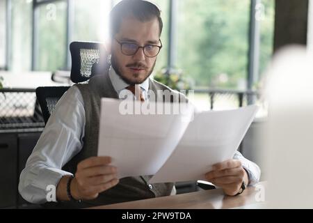 Satisfied man reading paper documents, letters, receiving pleasant news, working at workplace, sitting on desk, successful businessman, freelancer loo Stock Photo