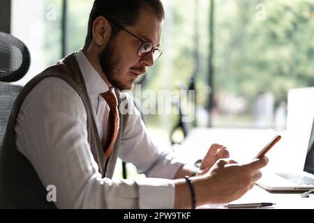 Engaged in work. Smiling businessman holding smartphone sitting in office. Middle aged manager ceo using cell phone mobile apps. Digital technology ap Stock Photo