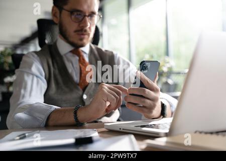 Engaged in work. Smiling businessman holding smartphone sitting in office. Middle aged manager ceo using cell phone mobile apps. Digital technology ap Stock Photo