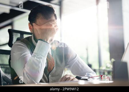 Feeling exhausted. Frustrated middle-aged beard man keeping eyes closed while sitting at his working place in office Stock Photo