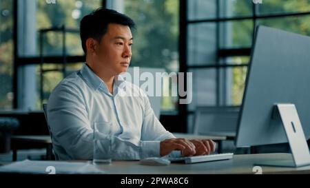 Professional male worker asian korean man successful businessman programmer specialist sit at office desk work with computer software program Stock Photo