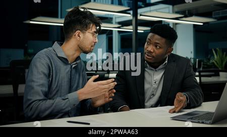 Diverse businessmen african american indian men talking discussing online project on computer sit at office desk two multiracial 30s male colleagues Stock Photo