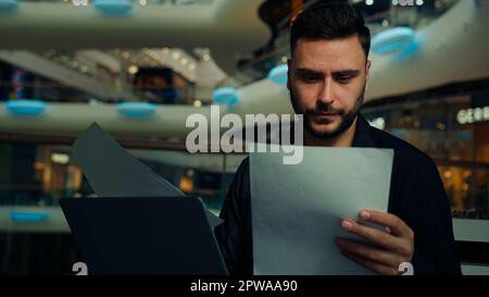 Male young businessman entrepreneur man doing corporate paperwork read business contract documentation paying bank loan bills online in banking app Stock Photo