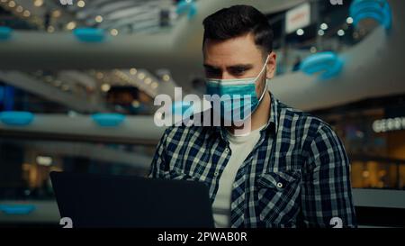 Young entrepreneur businessman student freelancer arabian hispanic man at shopping center in protective respirator mask chatting remote on internet Stock Photo