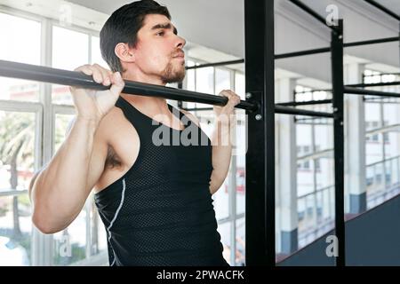 Sometimes the basic exercises are best. a young man doing pull ups in a gym. Stock Photo